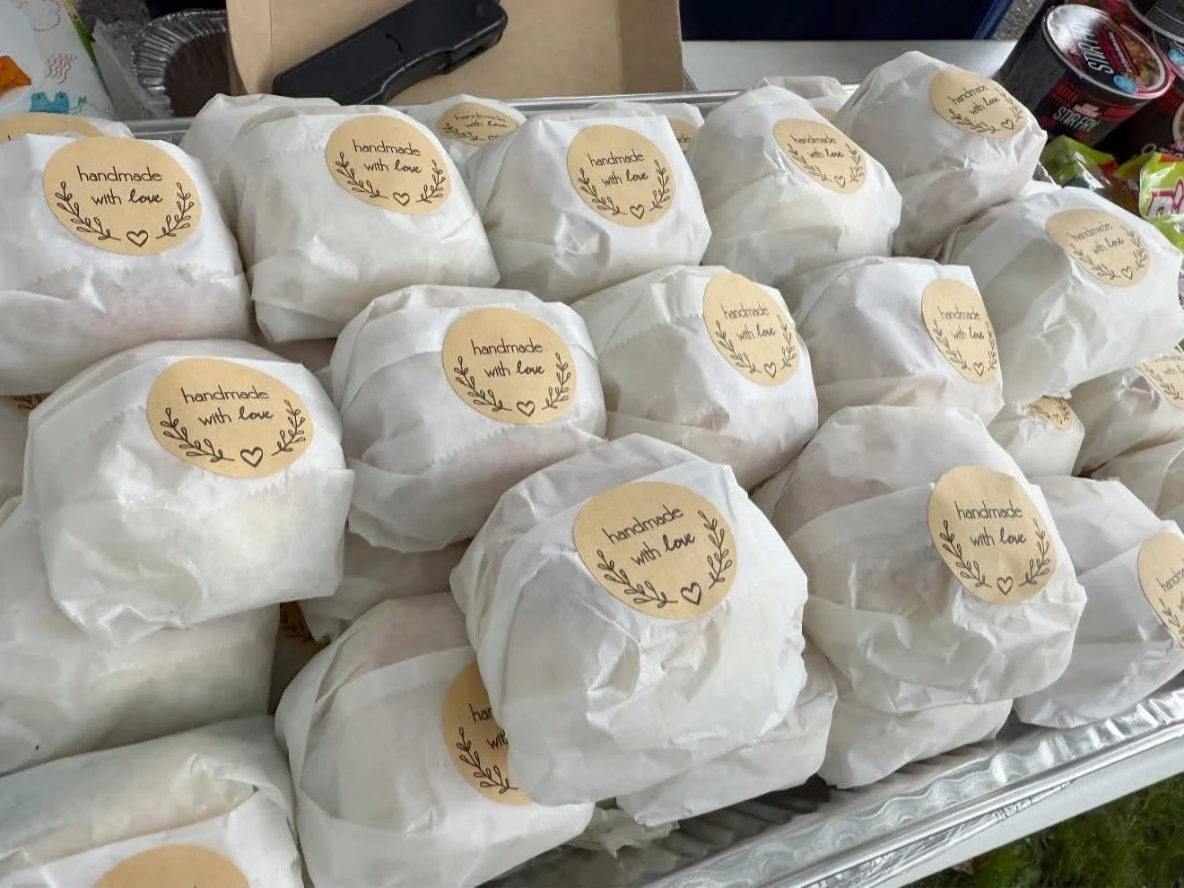 Multiple white wrapped items with beige round labels that read "handmade with love," located on a metal tray.