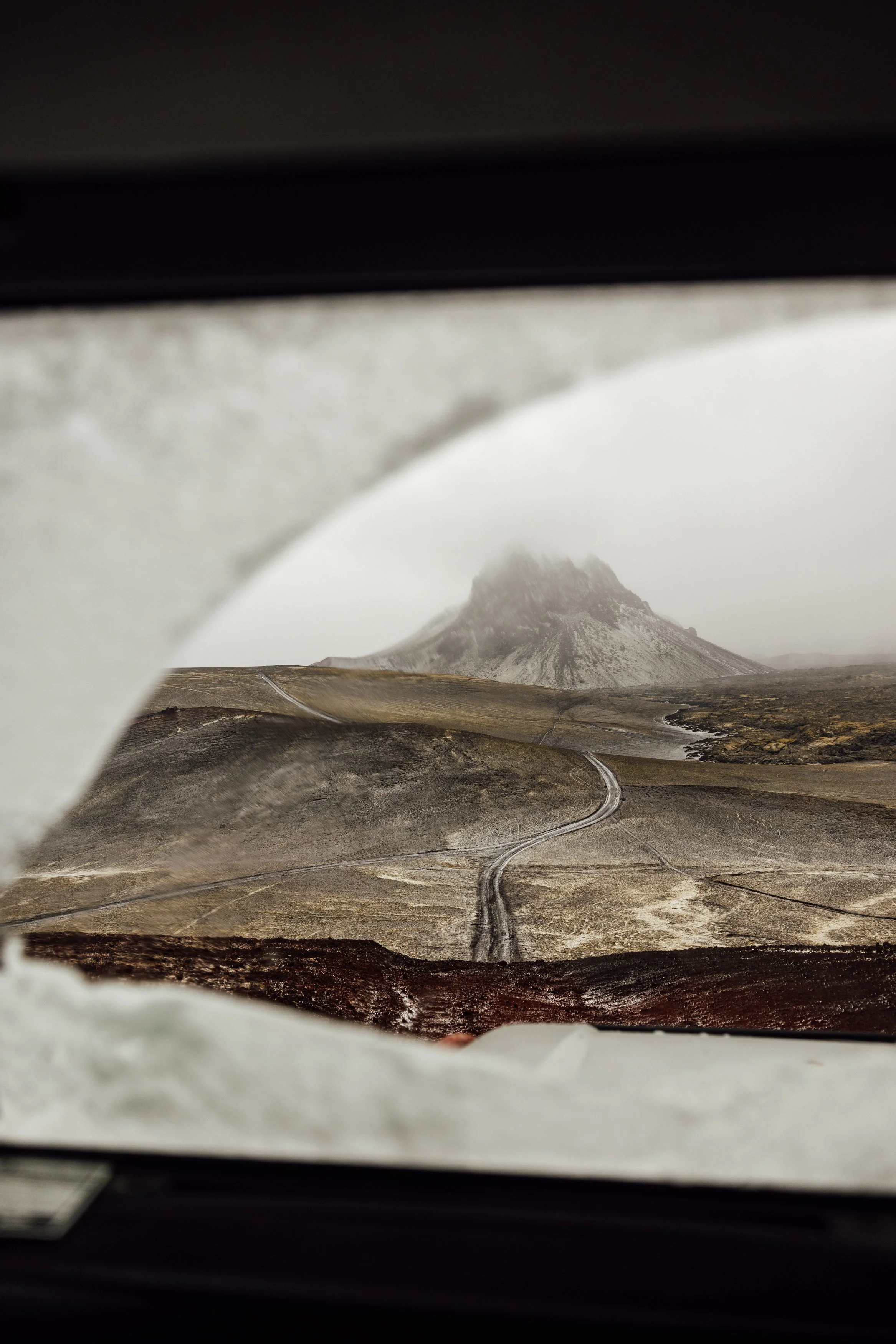 A distant mountain peak viewed through a car window with a winding road leading towards it.