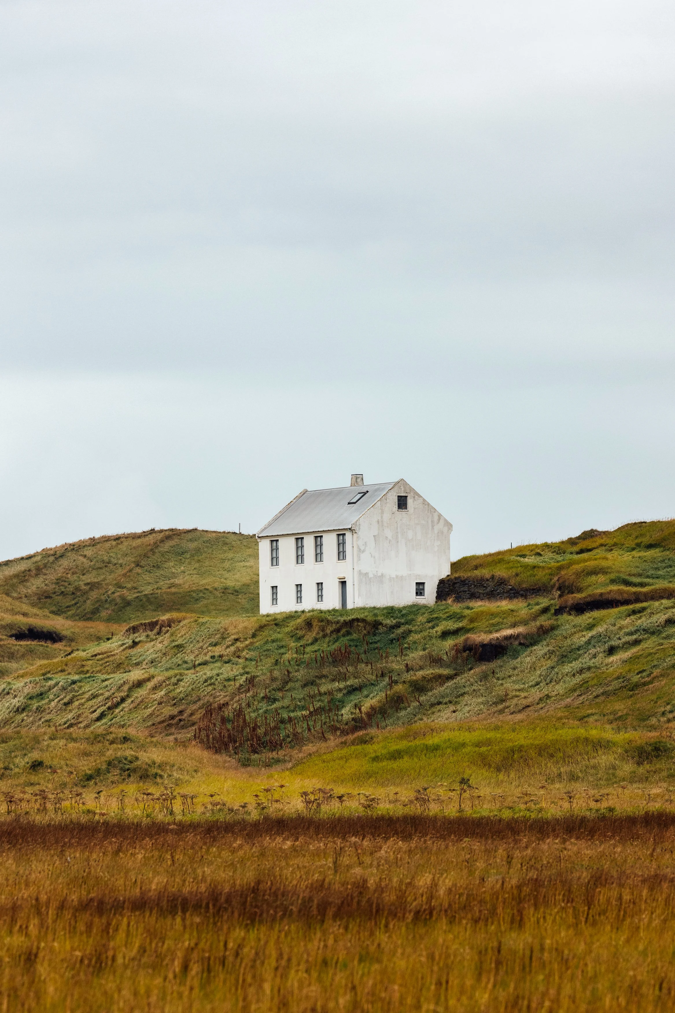 A white house perched on a green hillside with an overcast sky.