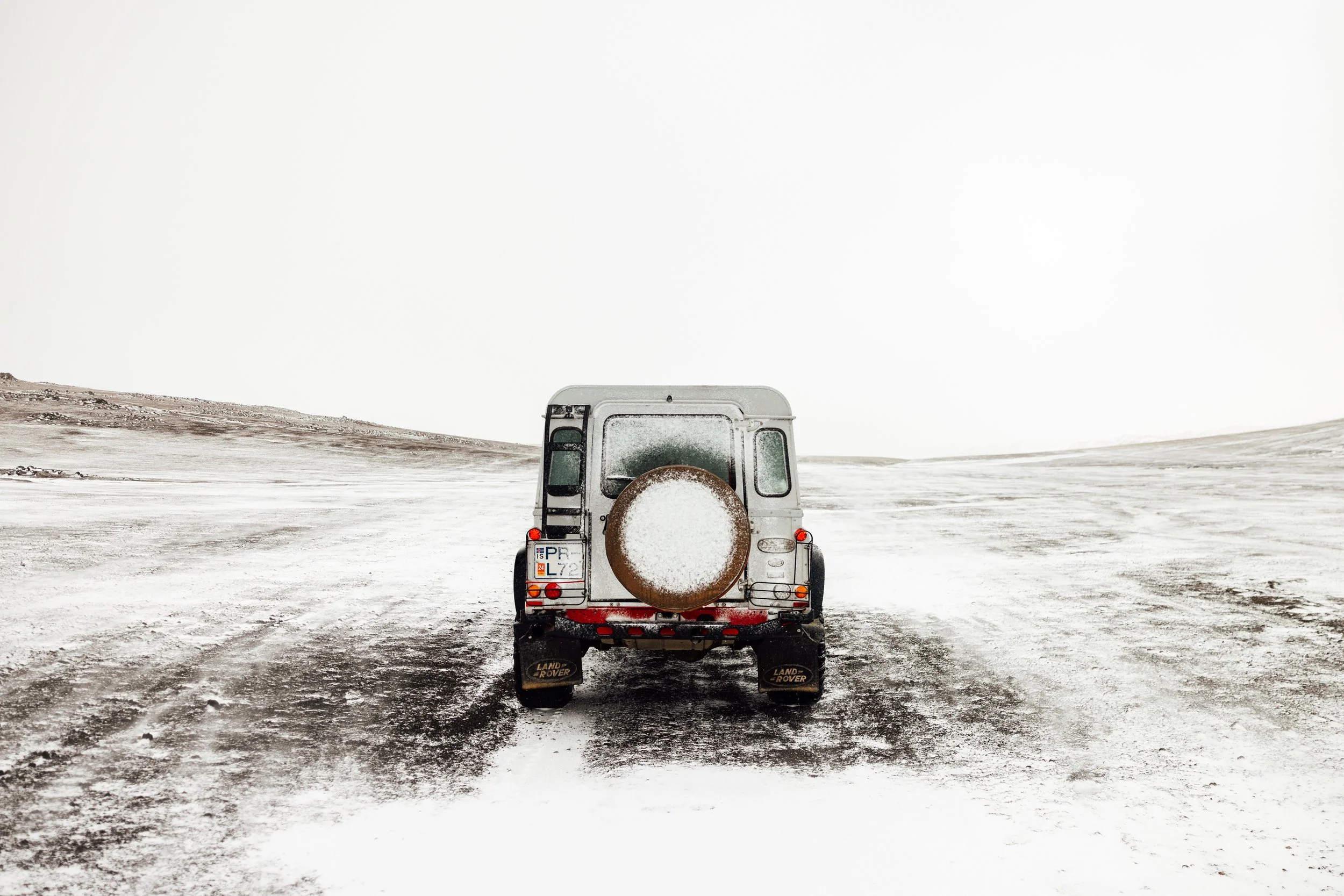 A land rover vehicle on a snow-covered, desolate landscape with a cloudy sky.
