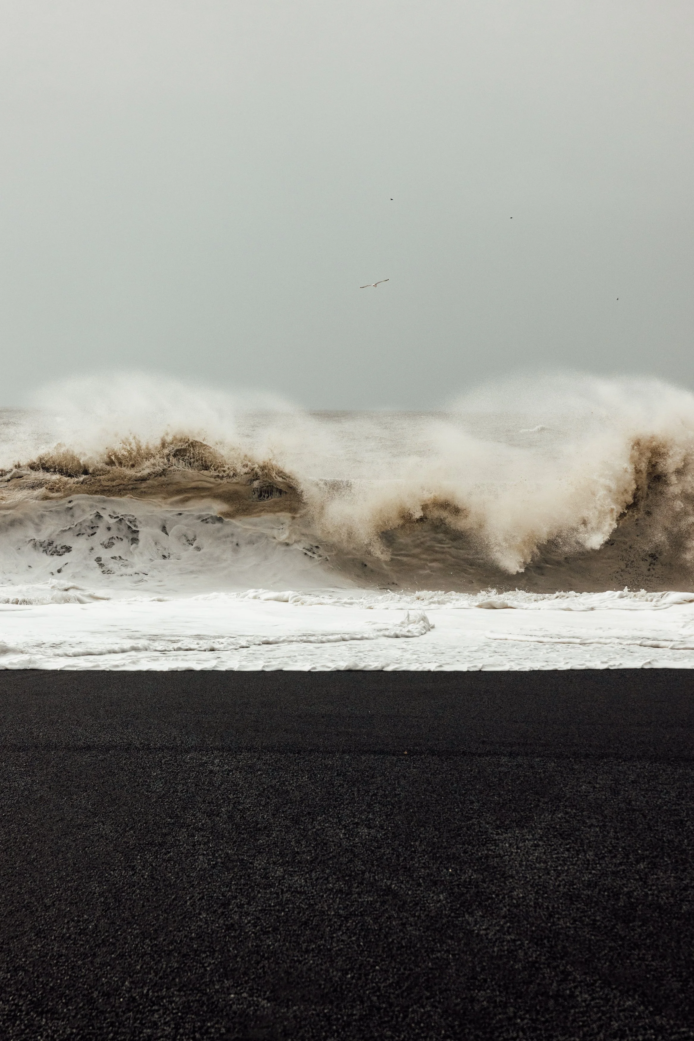Large ocean waves crashing onto a dark sandy beach on a cloudy day.