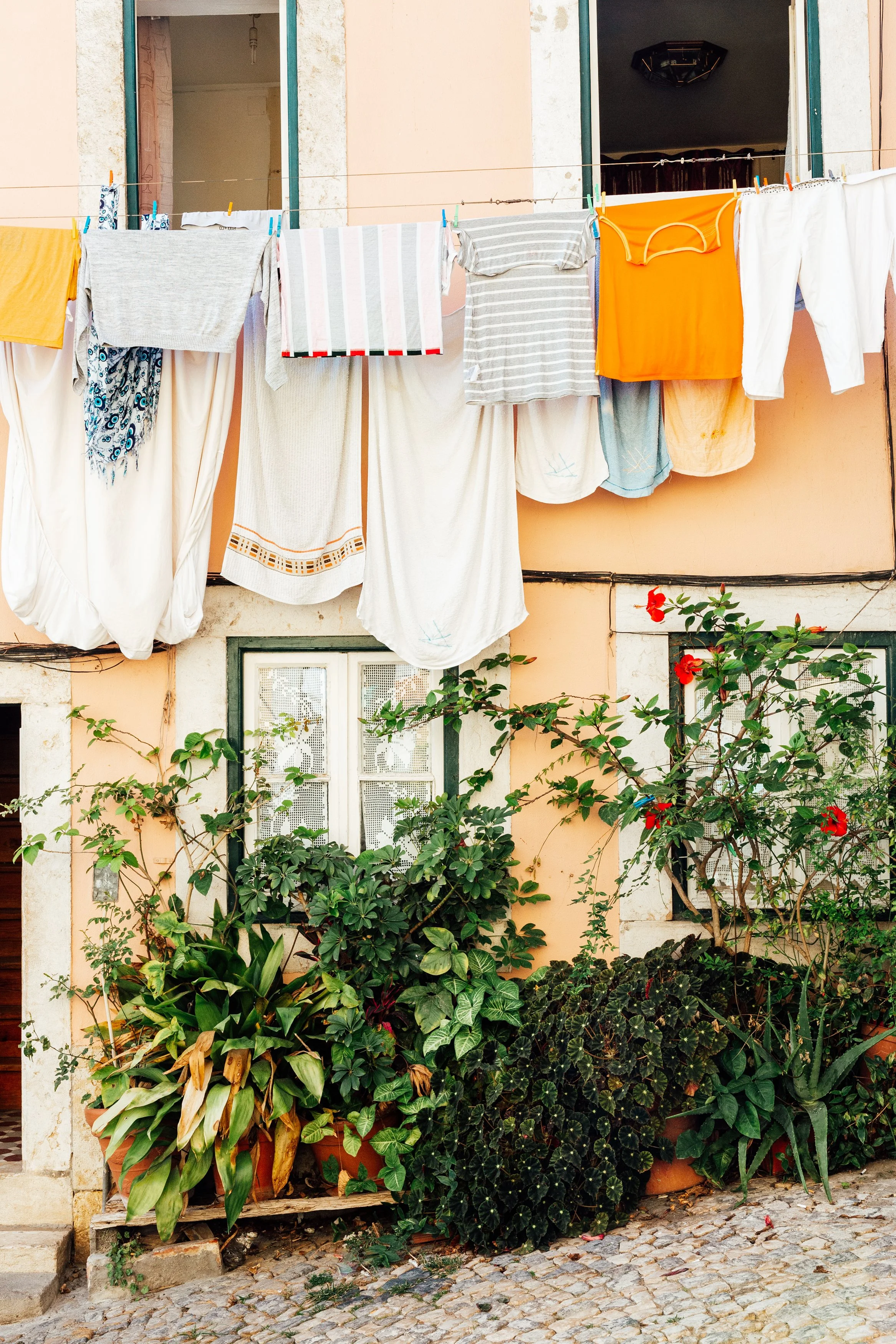 Clothes hanging on a laundry line outside a pink building with windows and plants below.