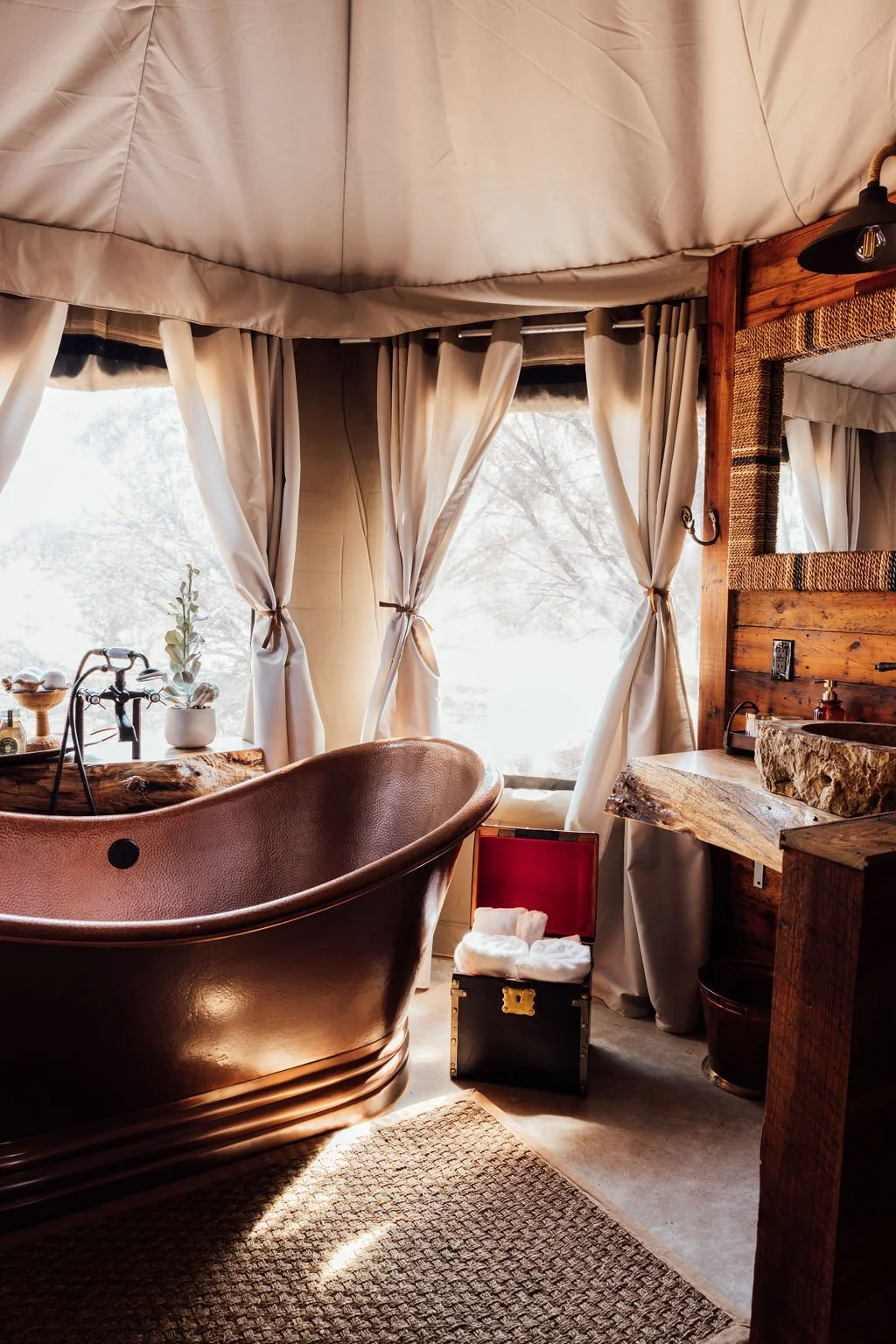 A cozy bathroom with a vintage bathtub, curtains, wooden accents, and a window letting in natural light.