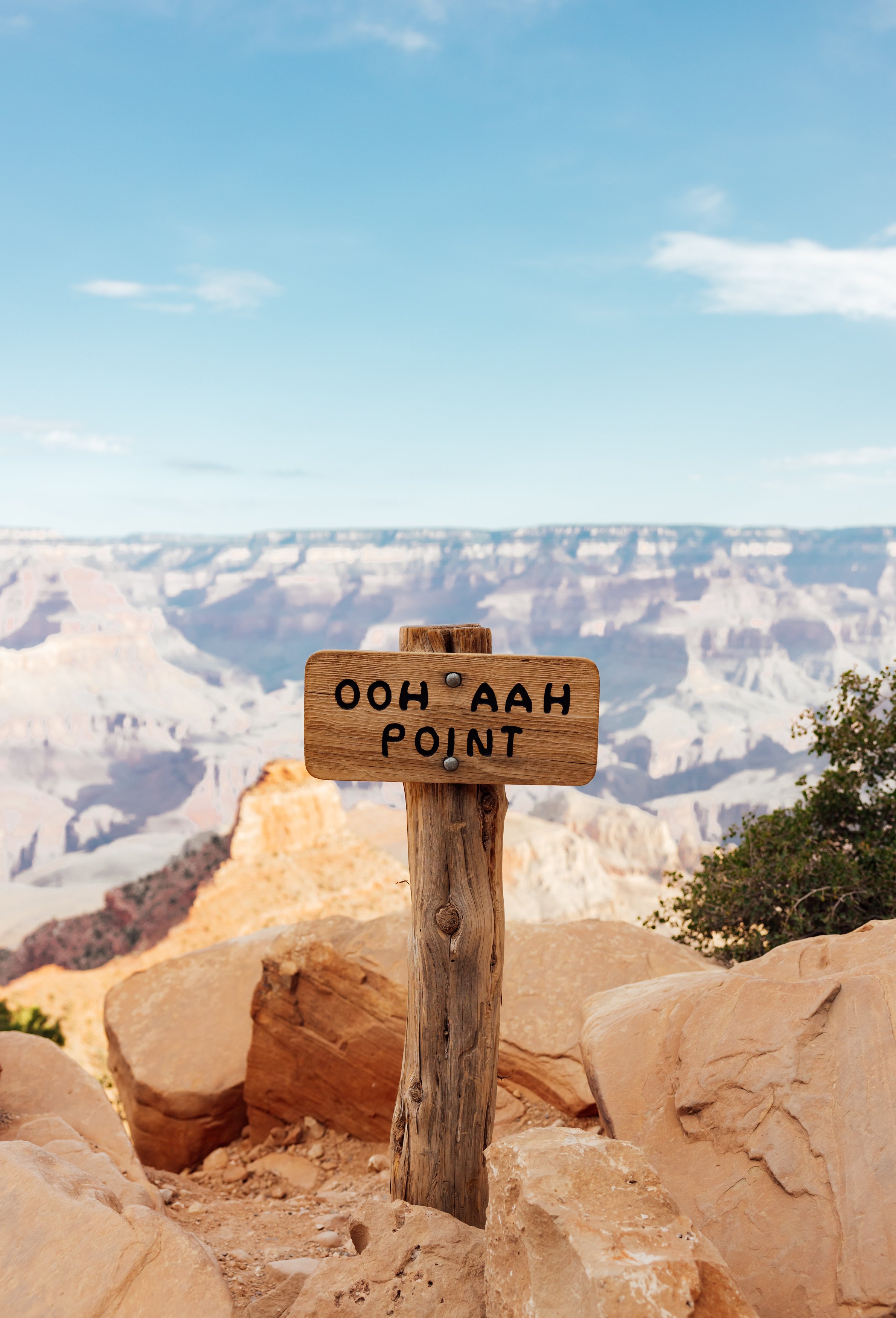 View of the Grand Canyon with a wooden sign that reads 'Ooh Aah Point' in the foreground.