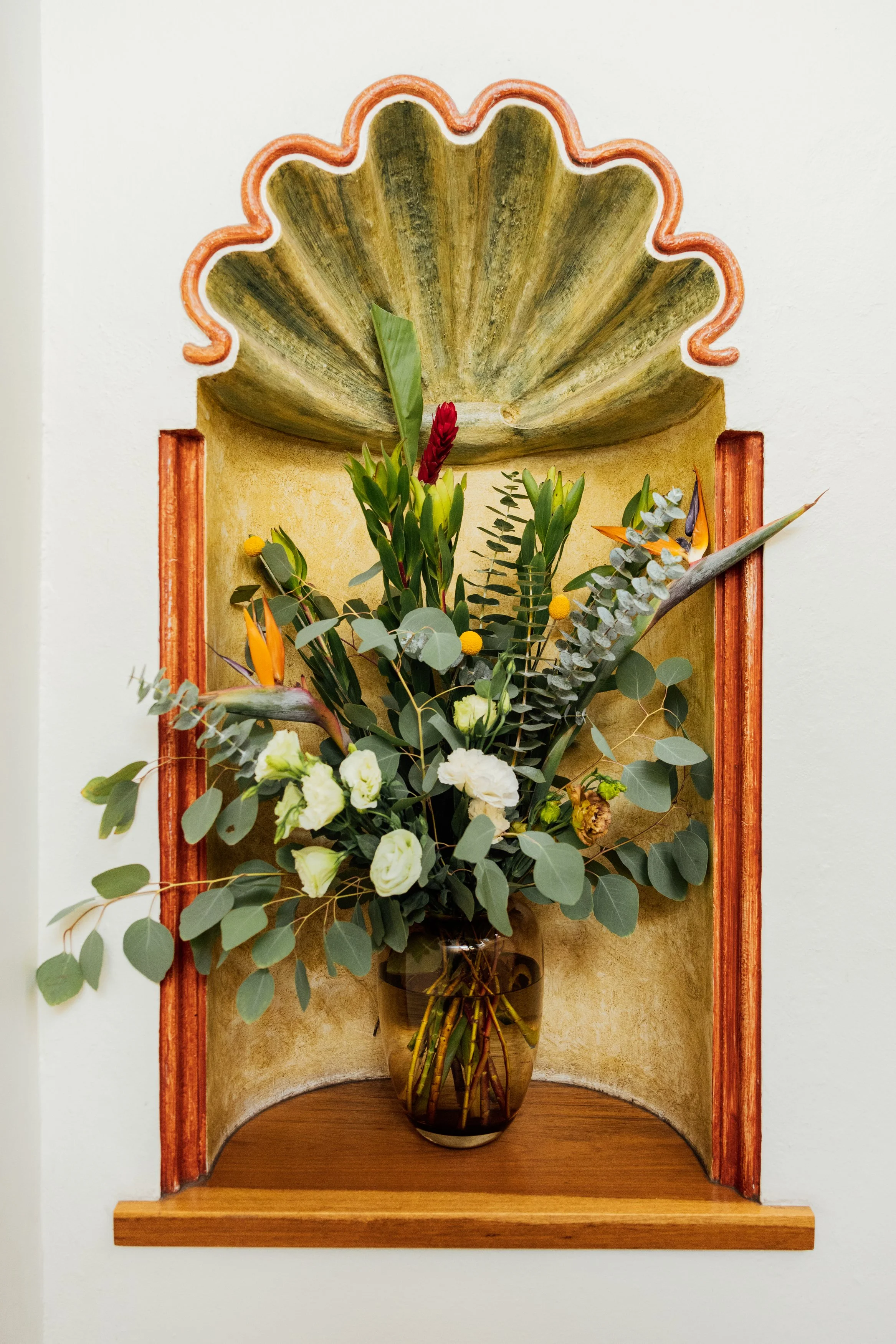 Decorative wall niche holding a glass vase with a floral arrangement of white, yellow, orange, and green flowers and foliage.