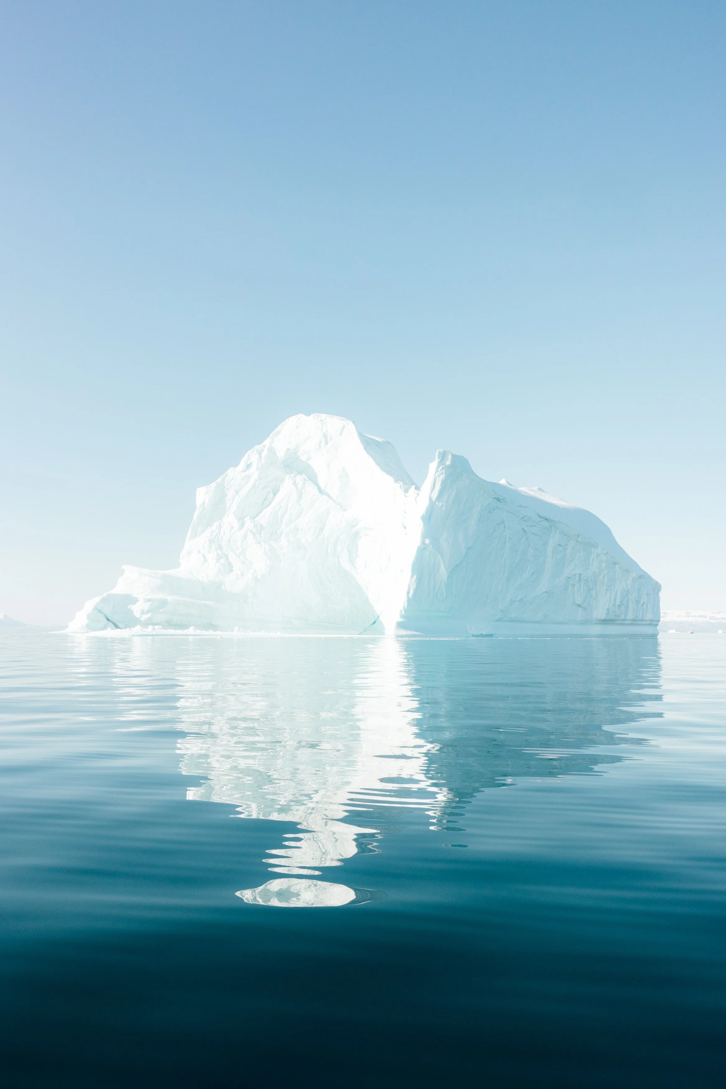 A large iceberg floating in calm ocean water under a clear blue sky.