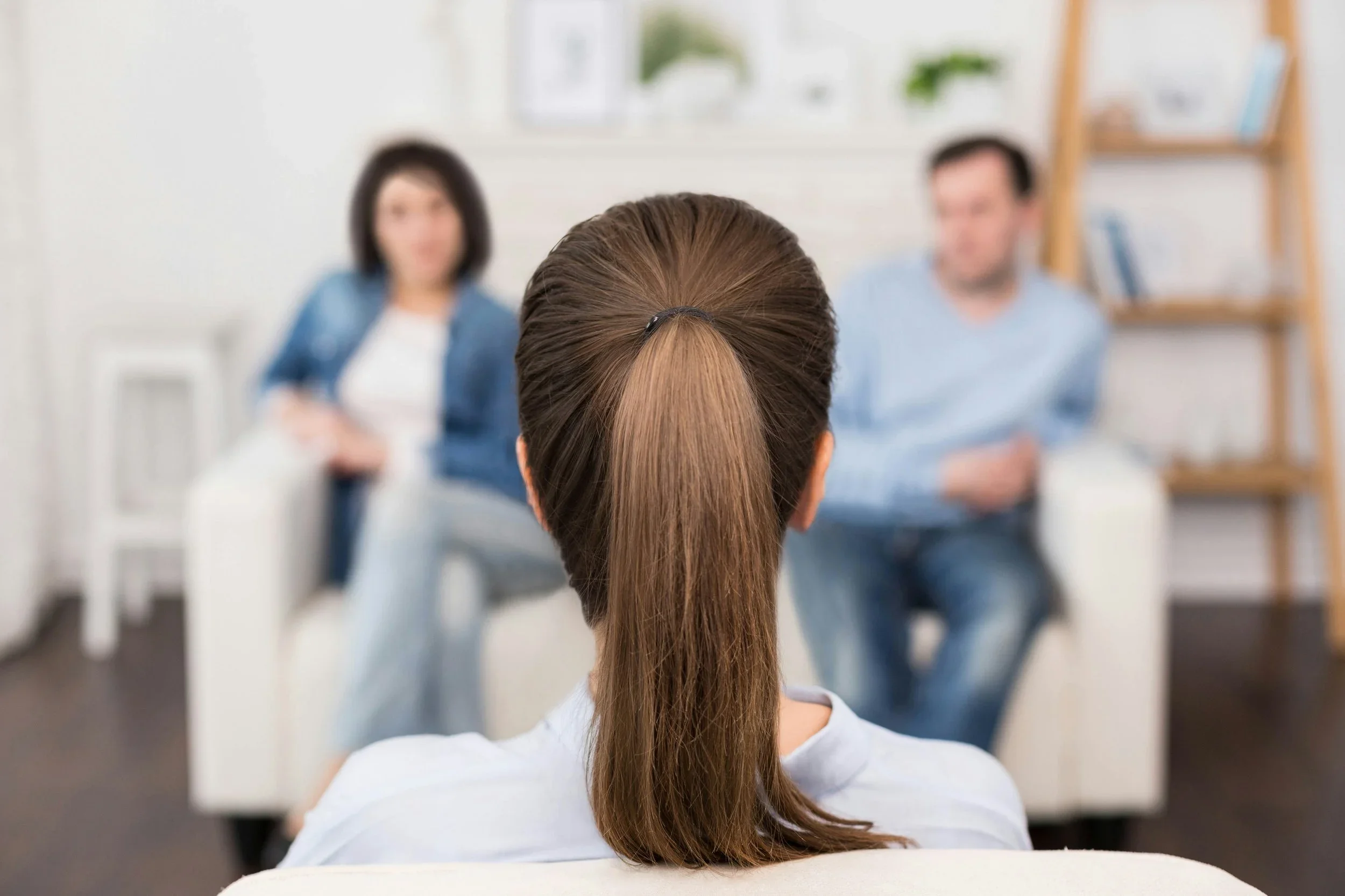 couple sitting in therapy office; therapist in forefront, couple in background, blurred. Depicting a couple therapy session.