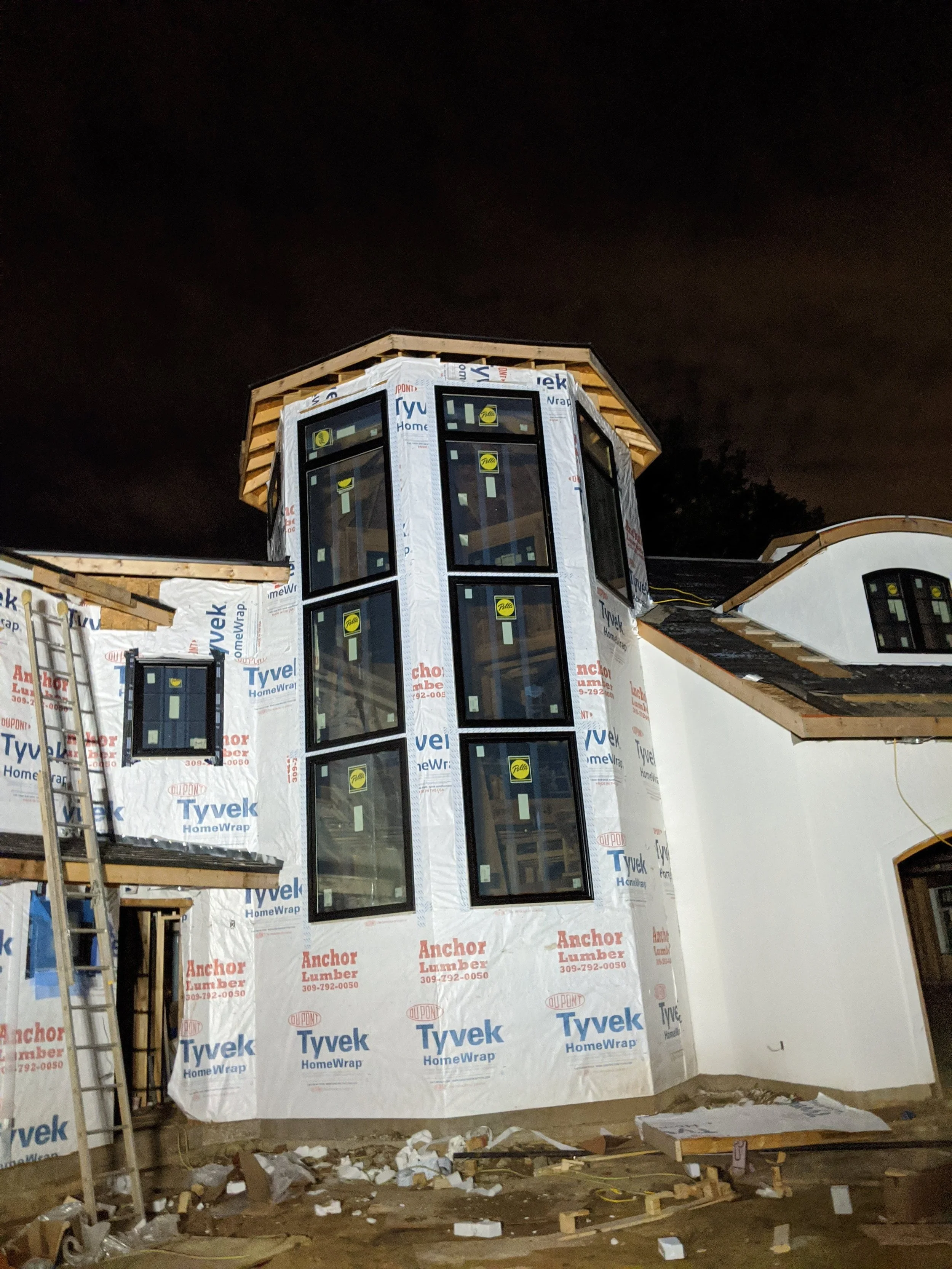 Tower in house wrap, lit by truck headlights during an evening push