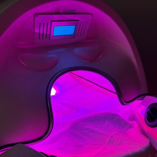 A red light therapy bed with a control display and two armrests.