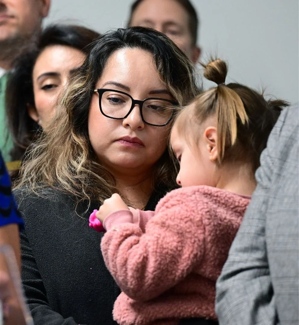 Woman holding a young child close, standing in a crowd