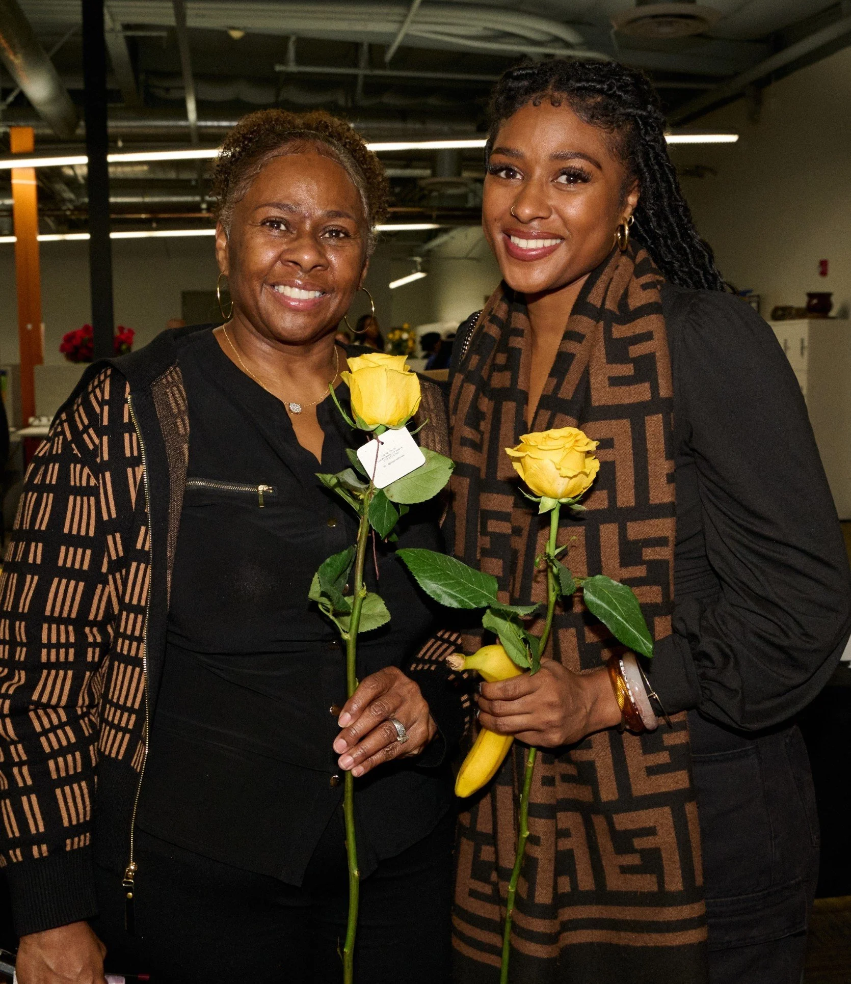Two women smiling together, each holding a yellow rose