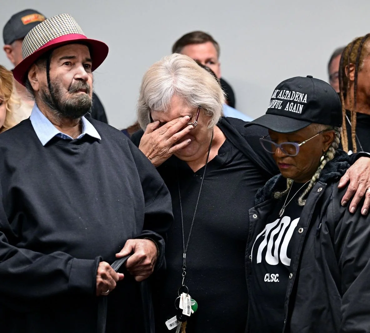 Three people standing together, one visibly emotional with hand over face, another wearing a 'Make Altadena Beautiful Again' cap