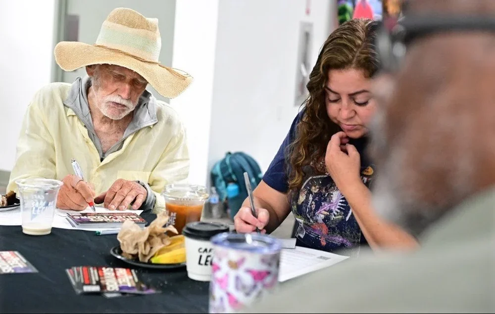 People filling out paperwork at a table with coffee and snacks nearby