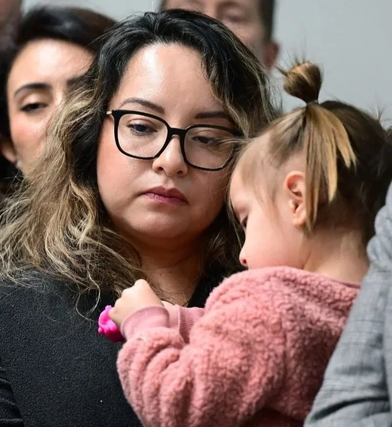 Woman holding a young child close, standing in a crowd