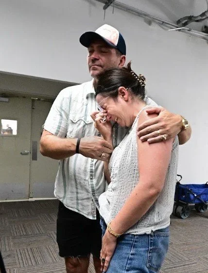 A woman crying while being comforted with an arm around her shoulder"