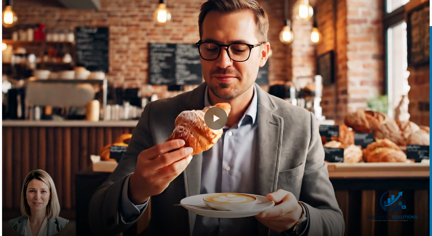 A man in glasses and a gray blazer holding a croissant and a cup of latte with foam art, inside a coffee shop with brick walls and hanging lights.