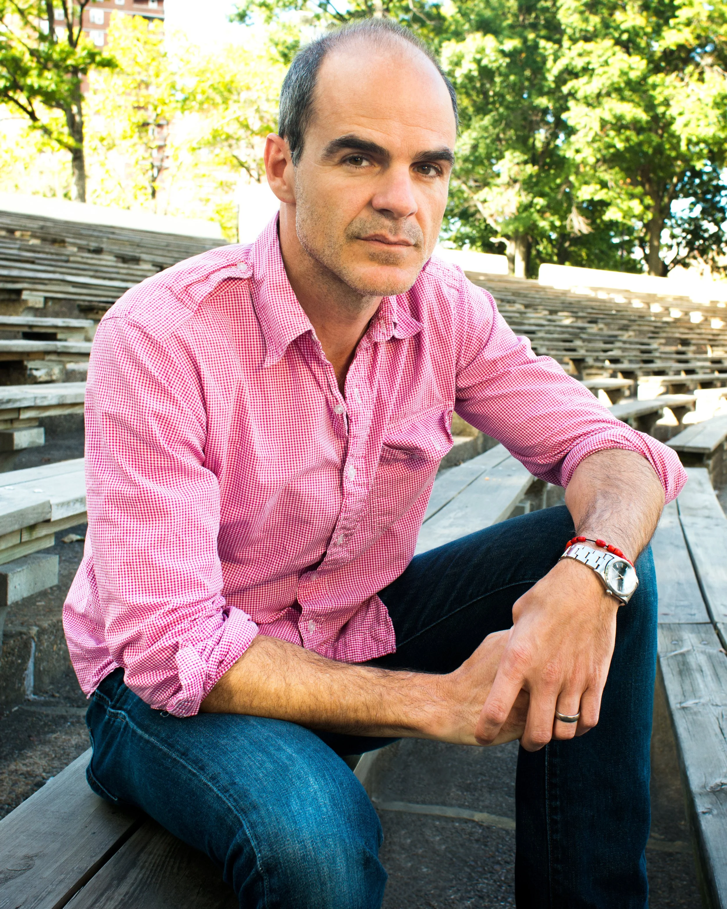 Man seated on outdoor bleachers in a pink shirt for a natural portrait session.