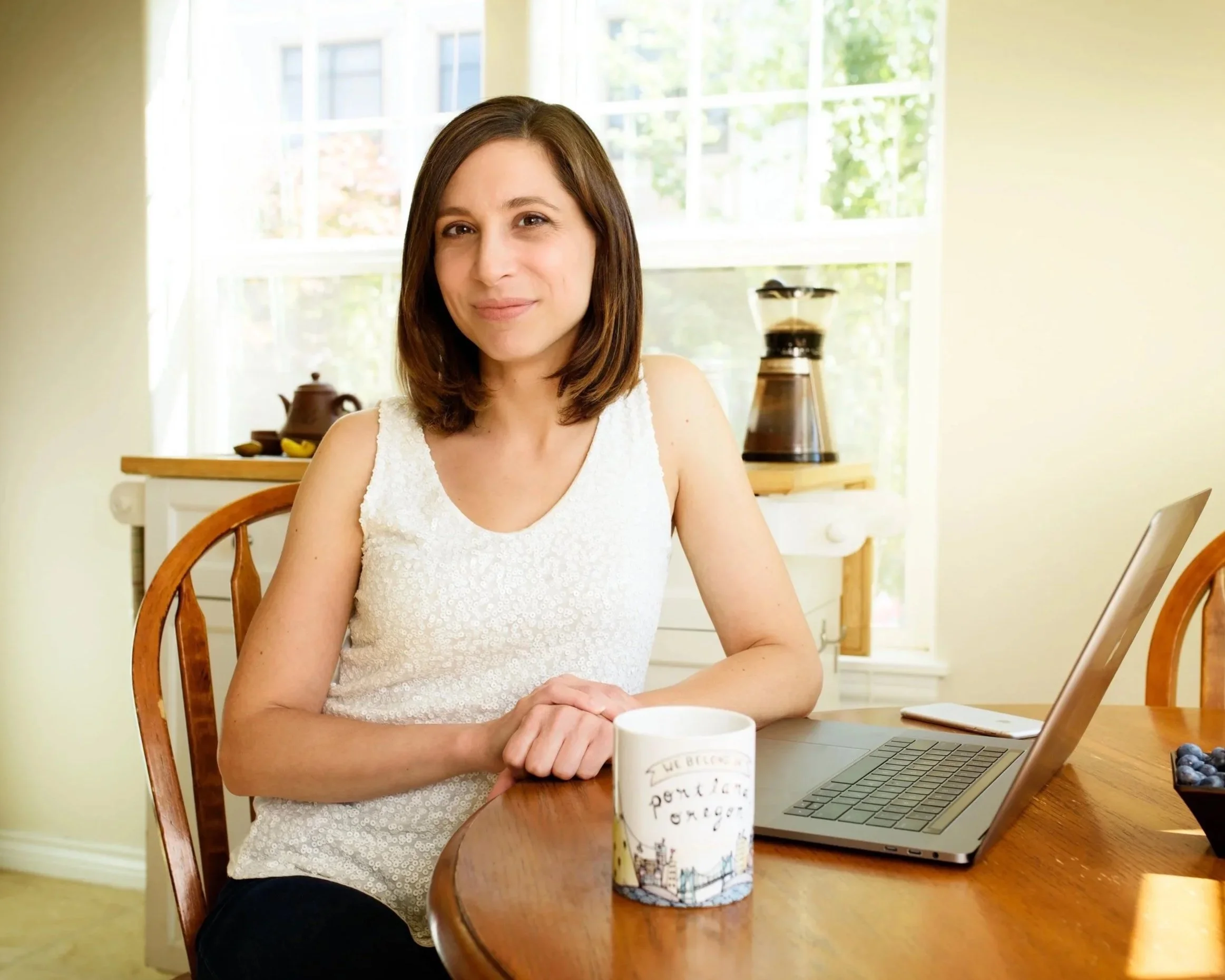 Woman seated at a kitchen table with a laptop for a natural branding portrait.