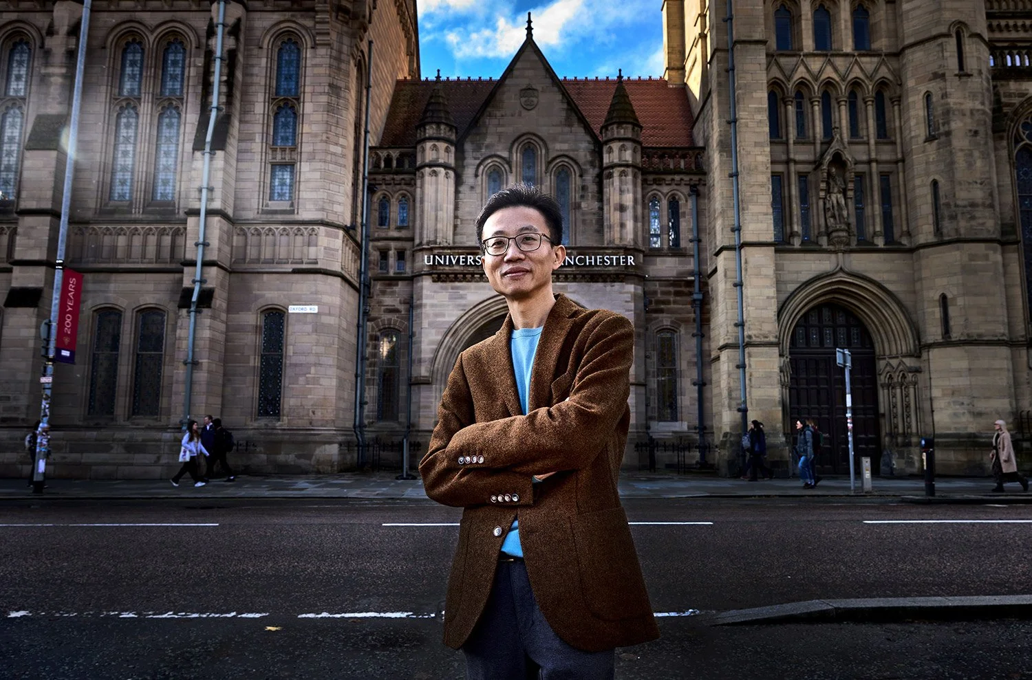 Corporate PR photograph of a professor standing outside the entrance to Manchester University by professional corporate editorial photographer Dave Phillips Photography
