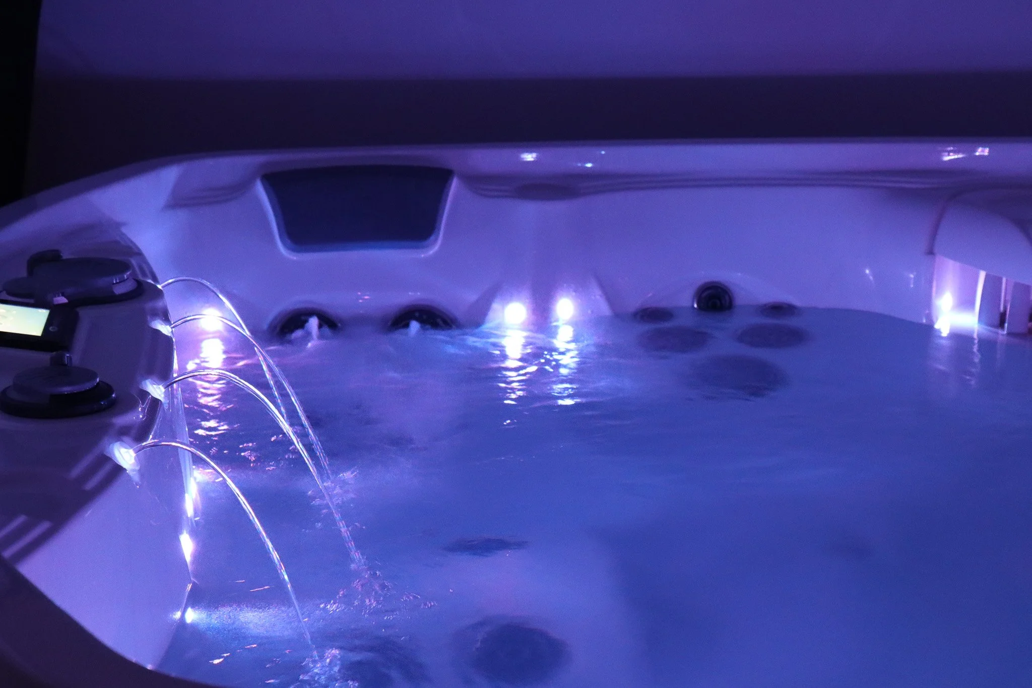 Photo d'une baignoire d'hydromassage avec des lumières bleues, des jets d'eau et un téléphone posé sur le rebord.