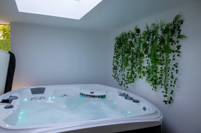 Un spa intérieur avec des jets d'eau, une fenêtre de toit, et une décoration murale de plantes vertes