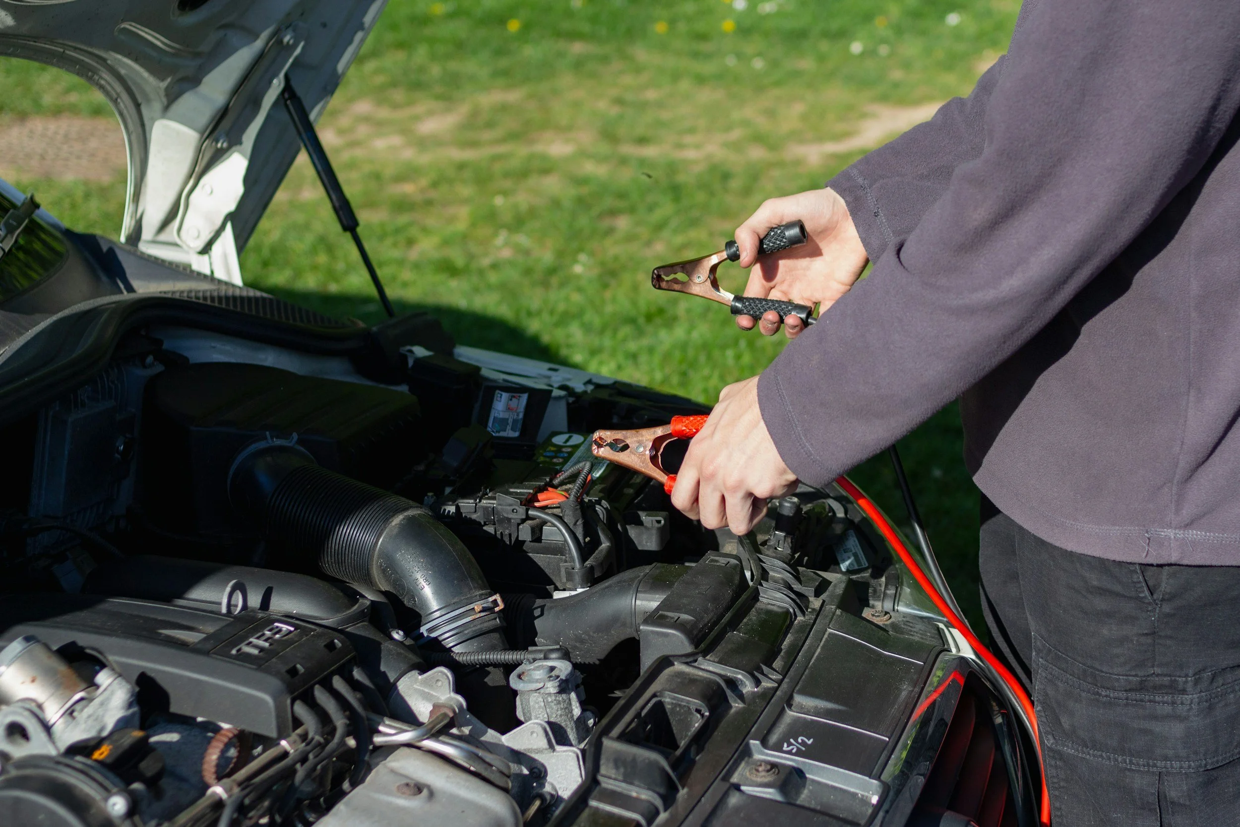 Person performing maintenance on a car engine using a wrench outside on a grassy area.