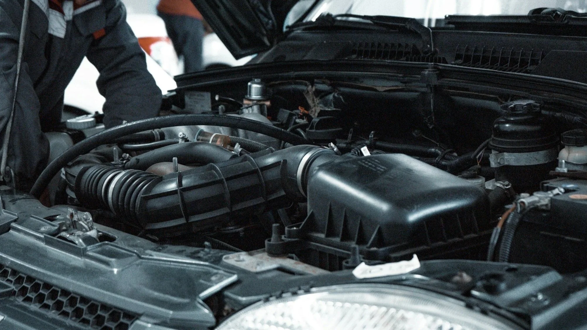 Close-up view of a car engine with a person working on it in the background.