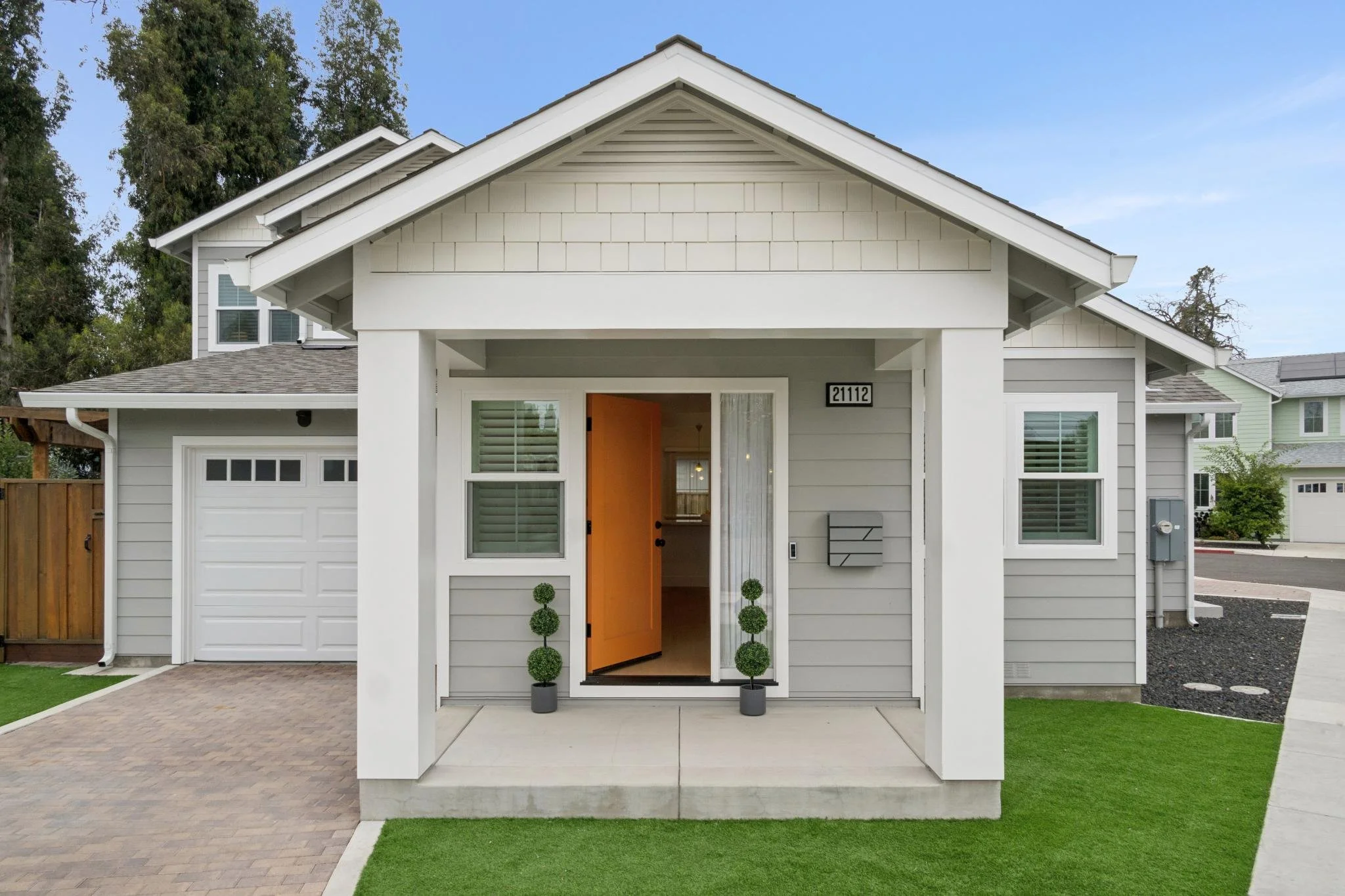 Front view of a modern house with a white porch, orange door, and green lawn.