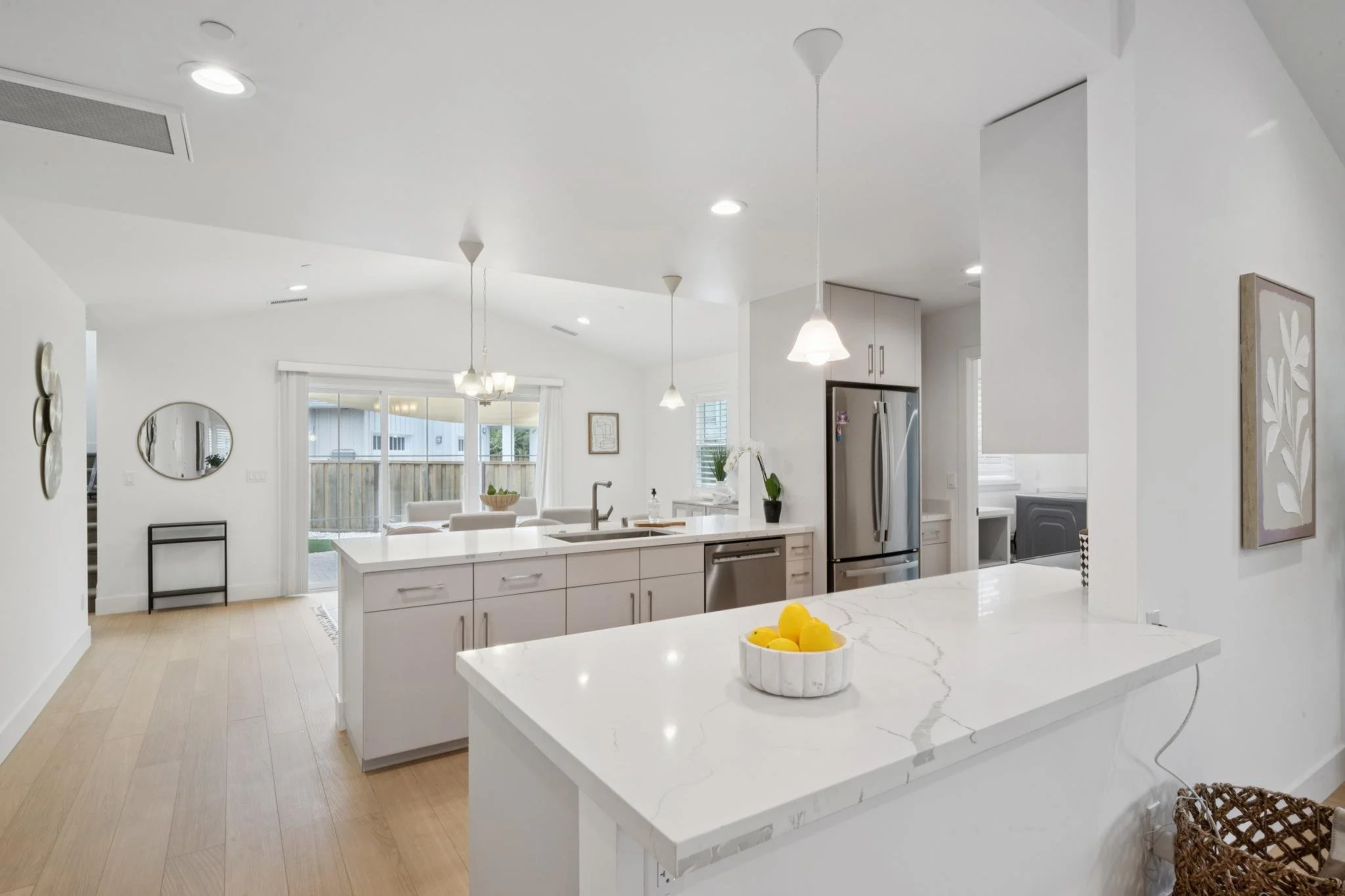 Modern kitchen with white cabinetry, marble countertops, pendant and recessed lighting, stainless steel refrigerator, and a breakfast bar with a bowl of lemons.