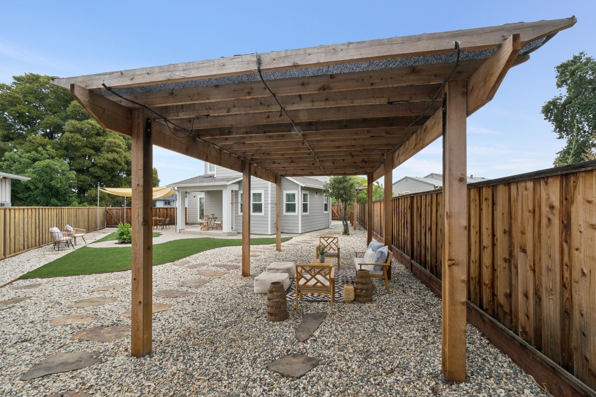 Backyard with a wooden pergola, outdoor seating, a lawn, gravel ground, a gravel pathway, and neighboring houses.