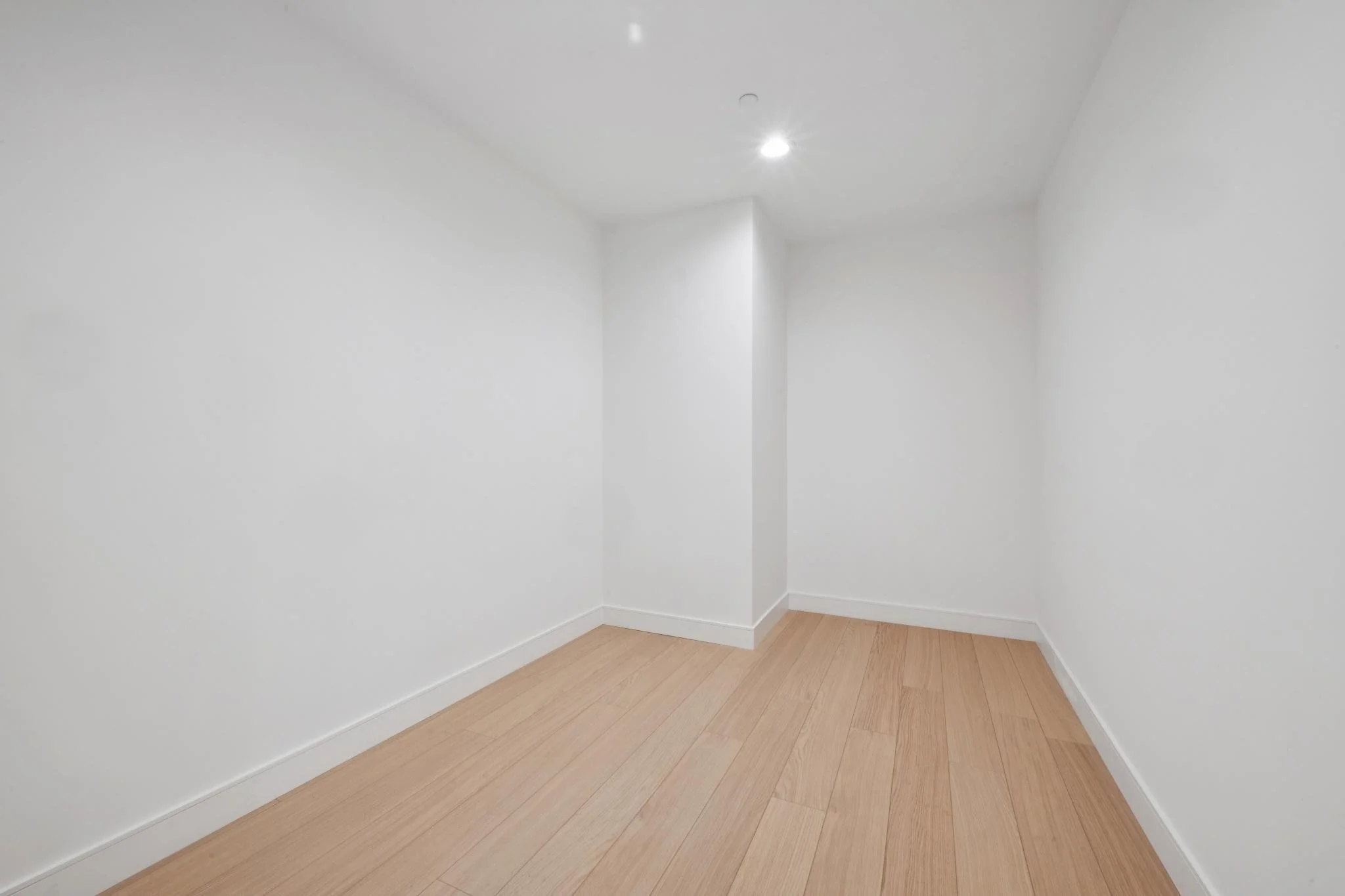 Empty white room with light wood flooring, white walls, and two ceiling lights.