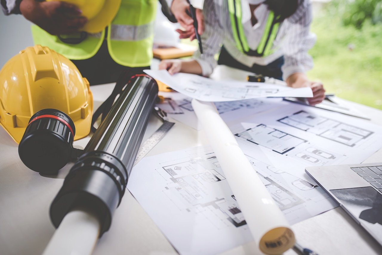 Architects or engineers reviewing blueprints and plans on a table, with construction helmets and measuring tools nearby.