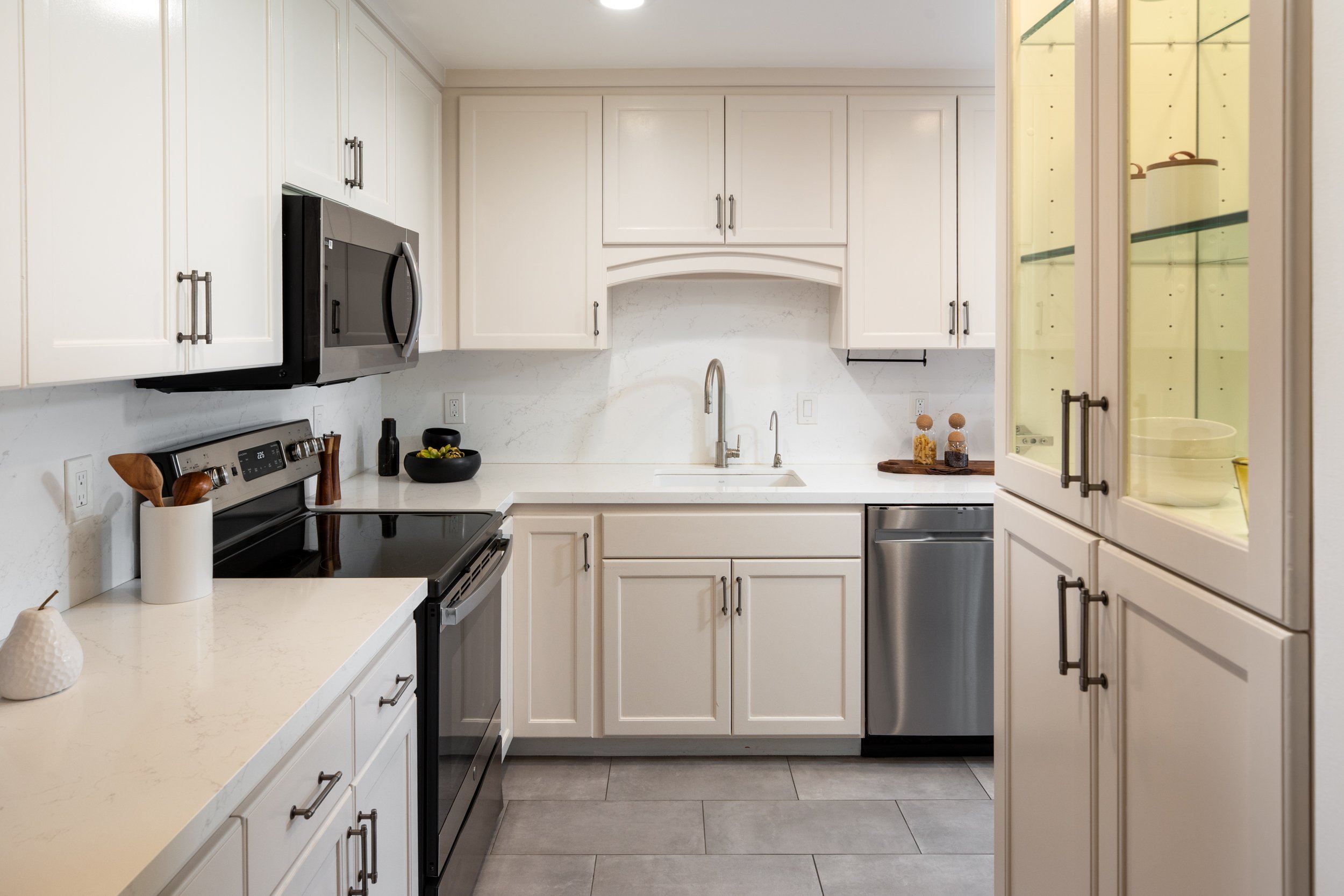 A modern white kitchen with beige cabinetry, stainless steel appliances, a marble backsplash, and decorative jars on the counter.