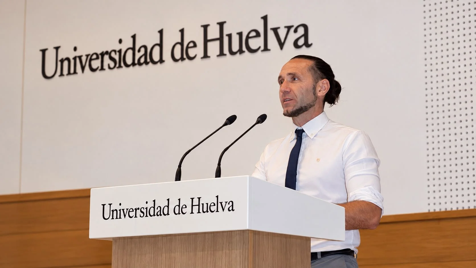 Man speaking at a podium labeled Universidad de Huelva