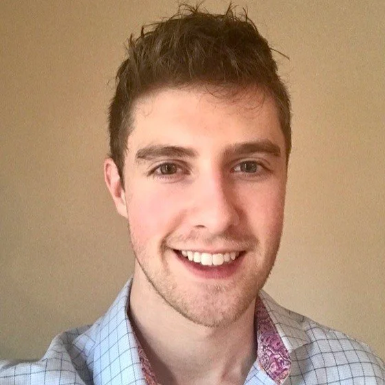 Smiling young man with short brown hair wearing a plaid shirt in a close-up portrait