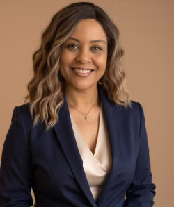 Professional headshot of a smiling woman with wavy brown hair wearing a navy blazer and cream blouse
