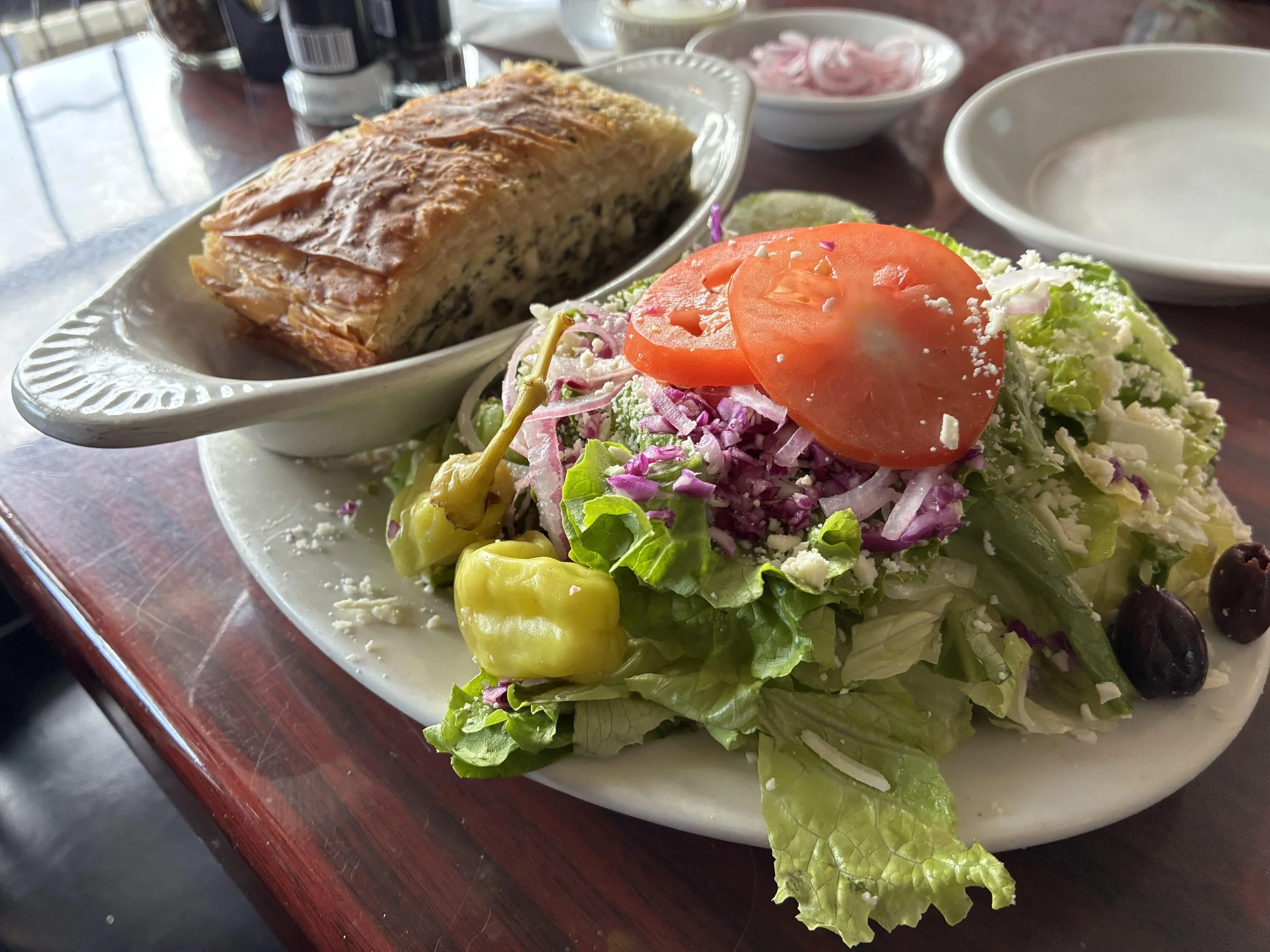 A plate with a slice of savory casserole and a side salad with sliced tomato, shredded cheese, and lettuce, on a dark wooden table.