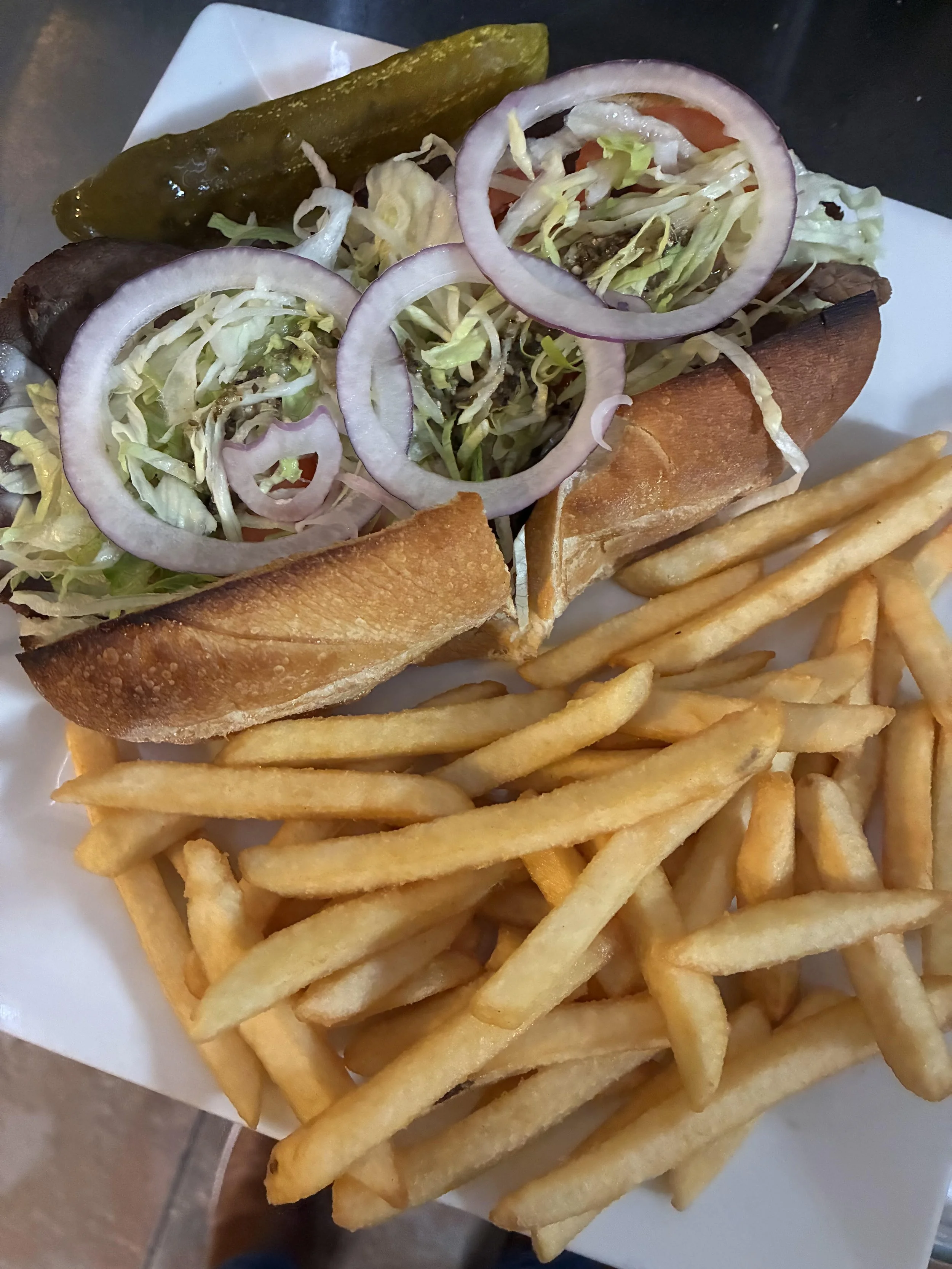 A hot dog bun with chopped lettuce, sliced red onions, tomato pieces, and pickles, served with a side of French fries.