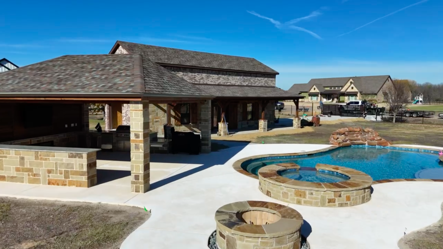 Real estate drone photography of a backyard pool, spa, stone fire pit, and covered pavilion at a Rockwall-area home