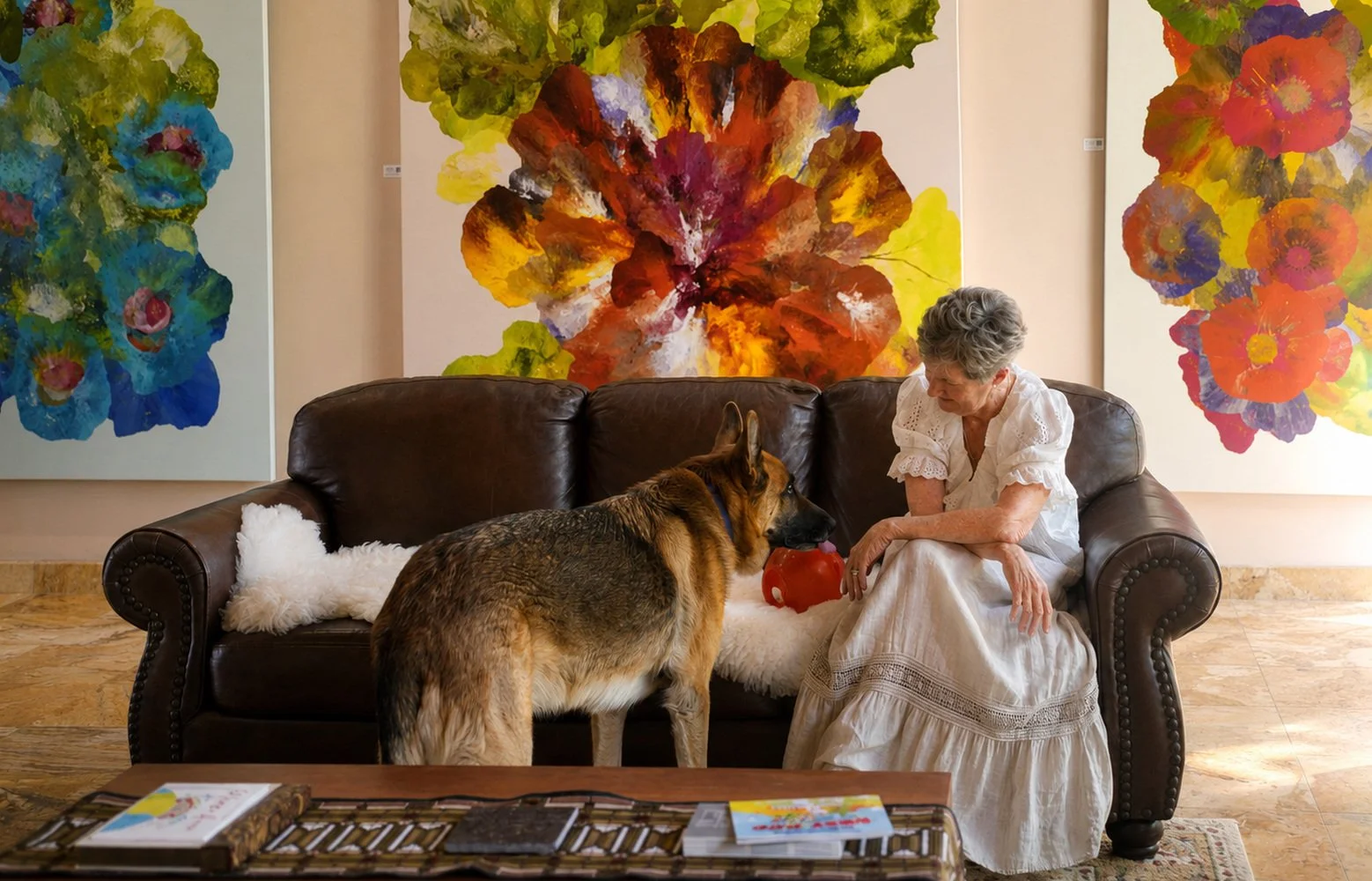 Artist seated with a dog in front of large-scale floral paintings.