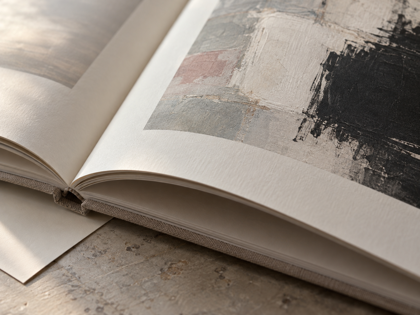 AI-generated process illustration: close-up of an open artist catalogue showing textured ivory paper, linen binding, and a printed abstract artwork.
