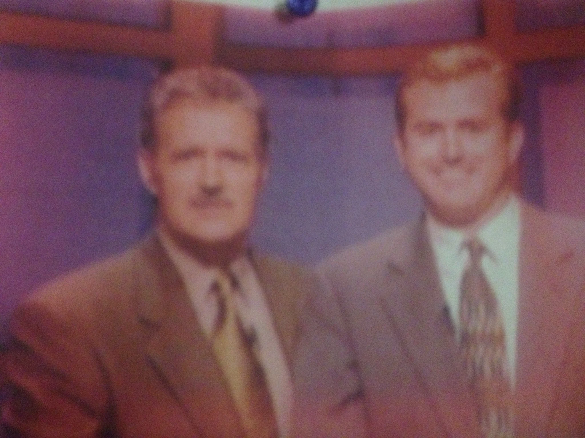 A blurry photo of two men in formal attire, standing side by side, with a purple background.
