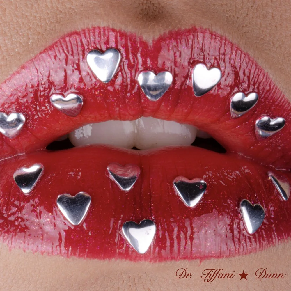 Close-up of lips with red lipstick and small silver heart-shaped studs on upper and lower lips.
