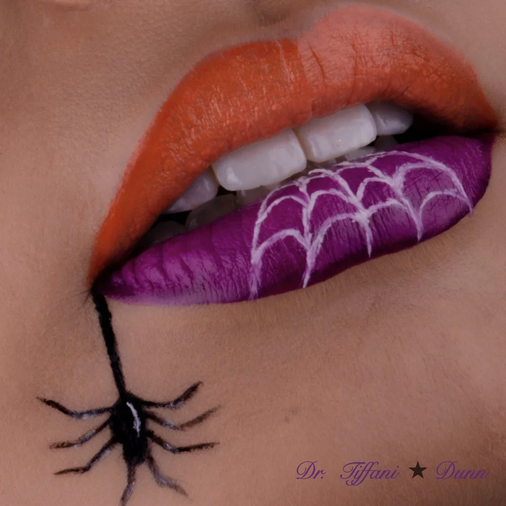 Close-up of lips painted orange and purple with a spider web design on the purple lipstick, and a small black spider hanging from the bottom lip. Text reads 'Dr. Tiffani Dunn' in purple cursive.