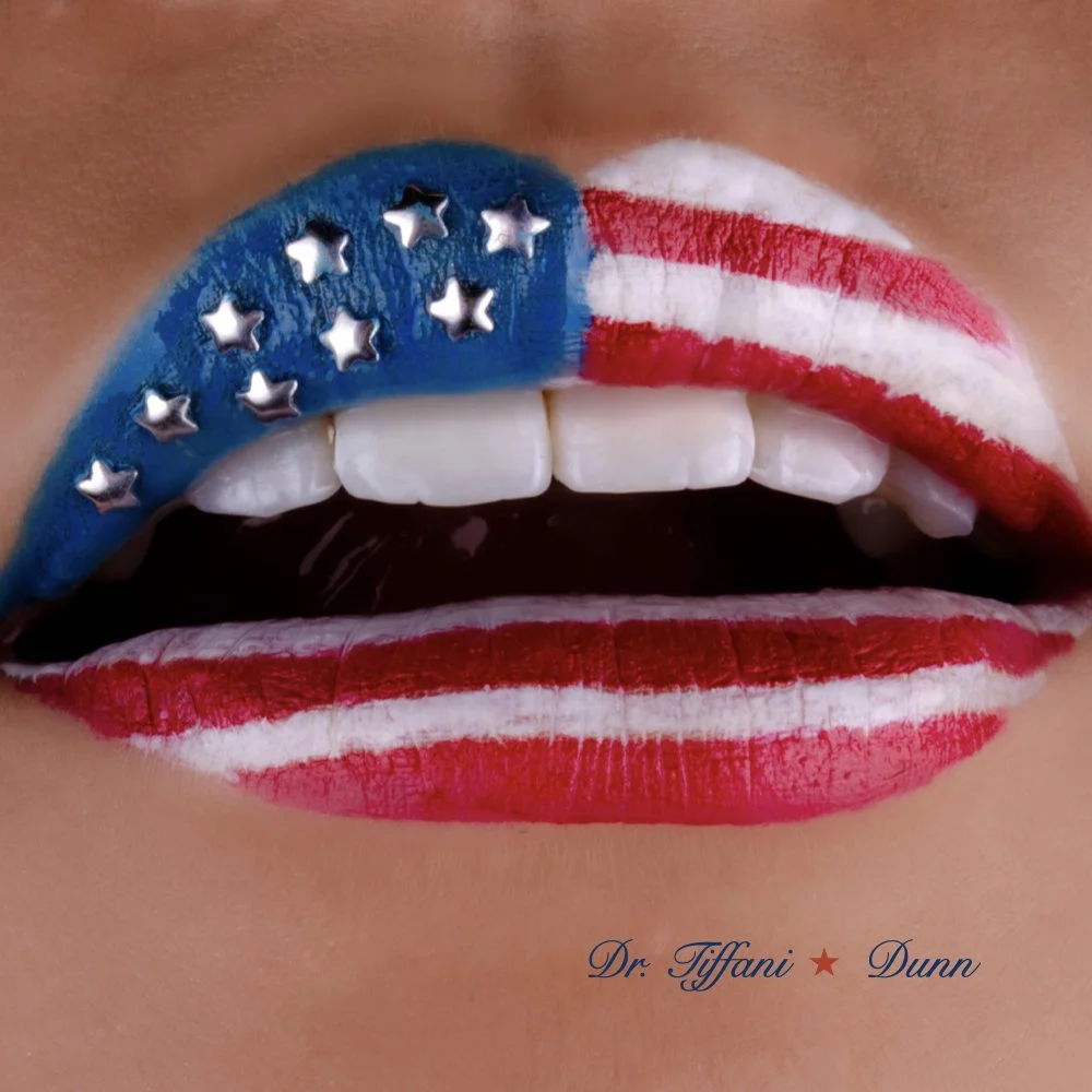 Close-up of lips painted with American flag design, with blue area with silver stars on one lip and red and white stripes on the other, with white teeth showing and a signature reading 'Dr. Tiffani Dunn' at the bottom.
