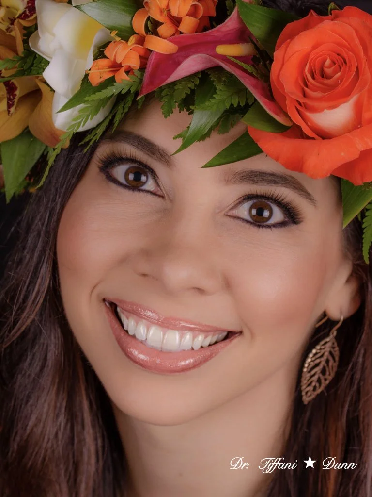 A woman smiling with a large flower crown including roses, lilies, and greenery.