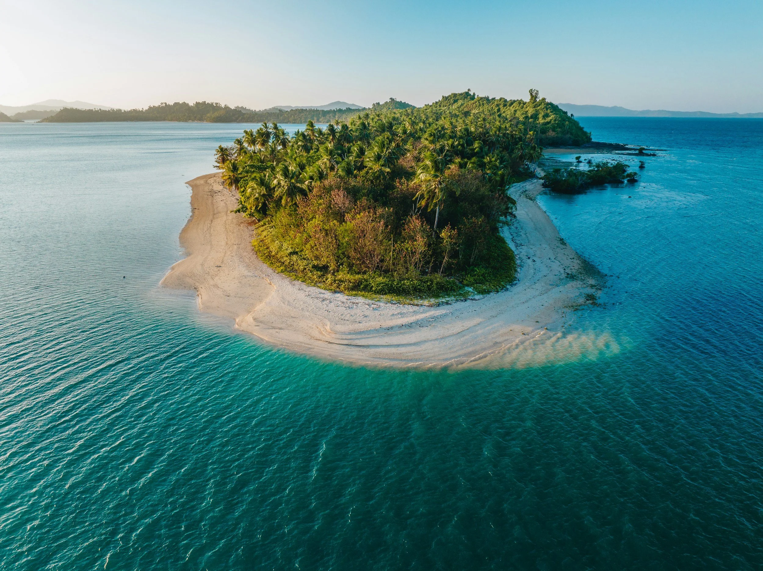 Aerial view of a sandy island with lush green vegetation surrounded by blue ocean waters.