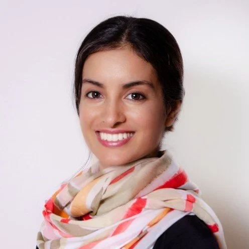 Close-up of a smiling woman with dark hair, wearing a patterned scarf, against a white background.