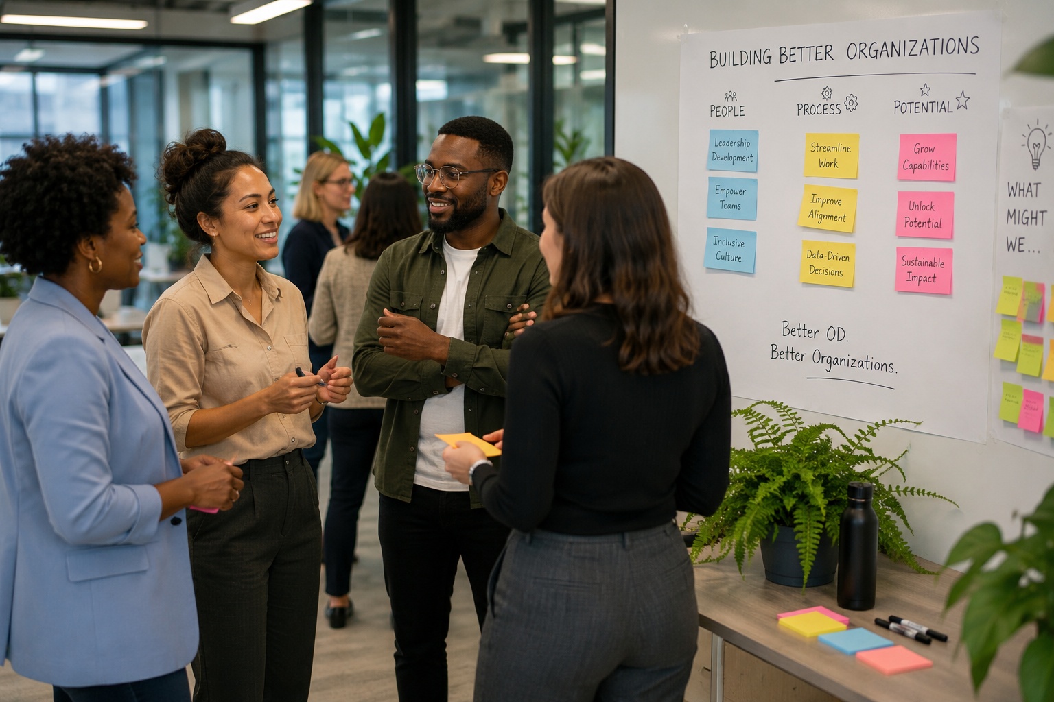 Group of four diverse colleagues having a discussion in front of a whiteboard with sticky notes and organizational goals, in a modern office setting.