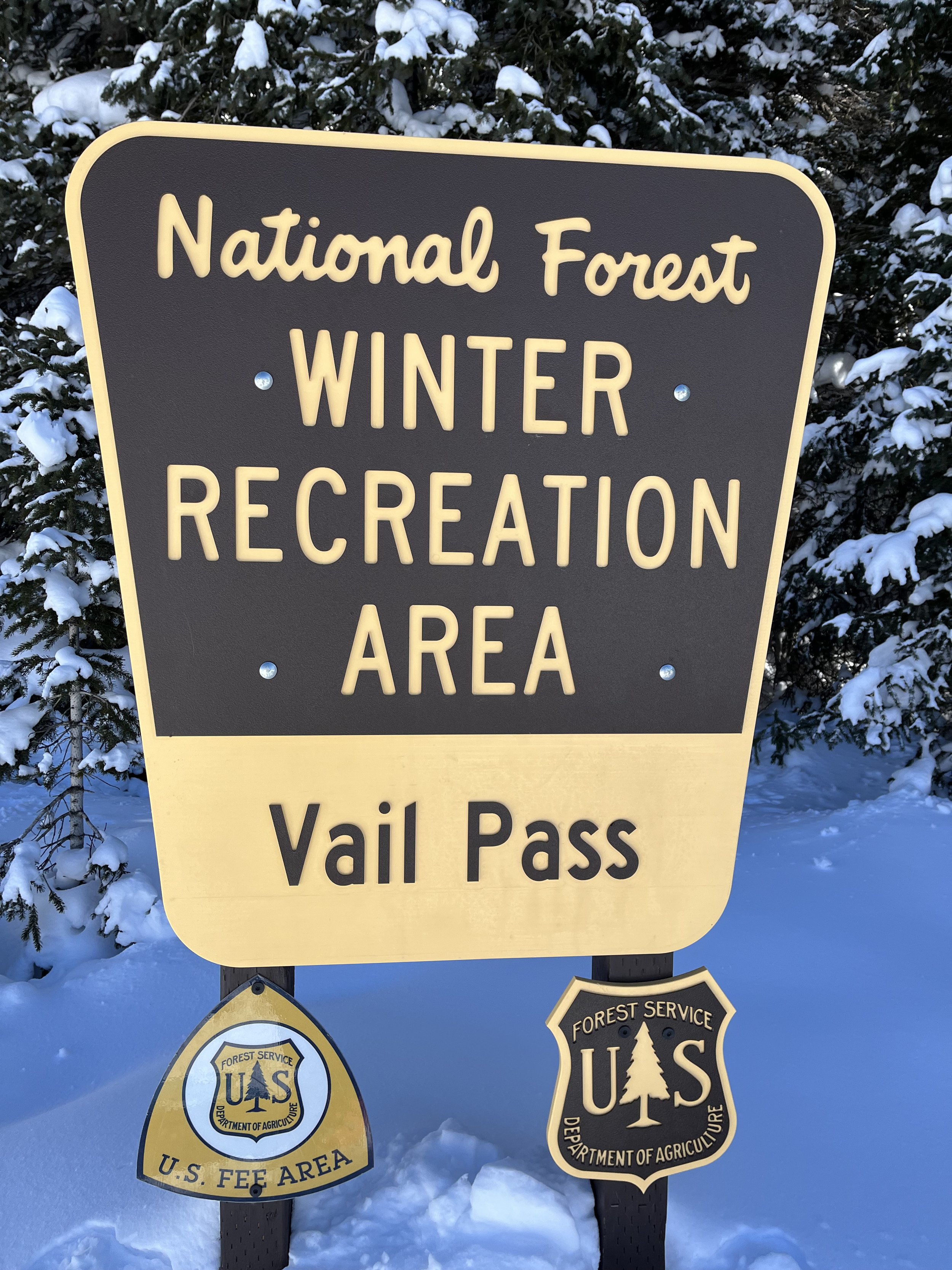Sign indicating the entrance to the National Forest Winter Recreation Area, with U.S. Forest Service badges for U.S. Forest Preserve and Department of Agriculture, in a snowy environment.